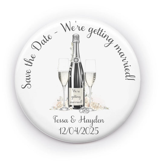 Save the date badge mirror featuring an image of champagne and glasses and personalised with names and wedding date.