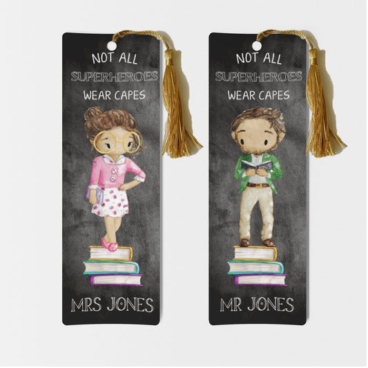 Aluminium bookmark with a gold tassel and featuring a male or female teacher standing on books. Text reads 'Not all superheroes wear capes' Can be personalised