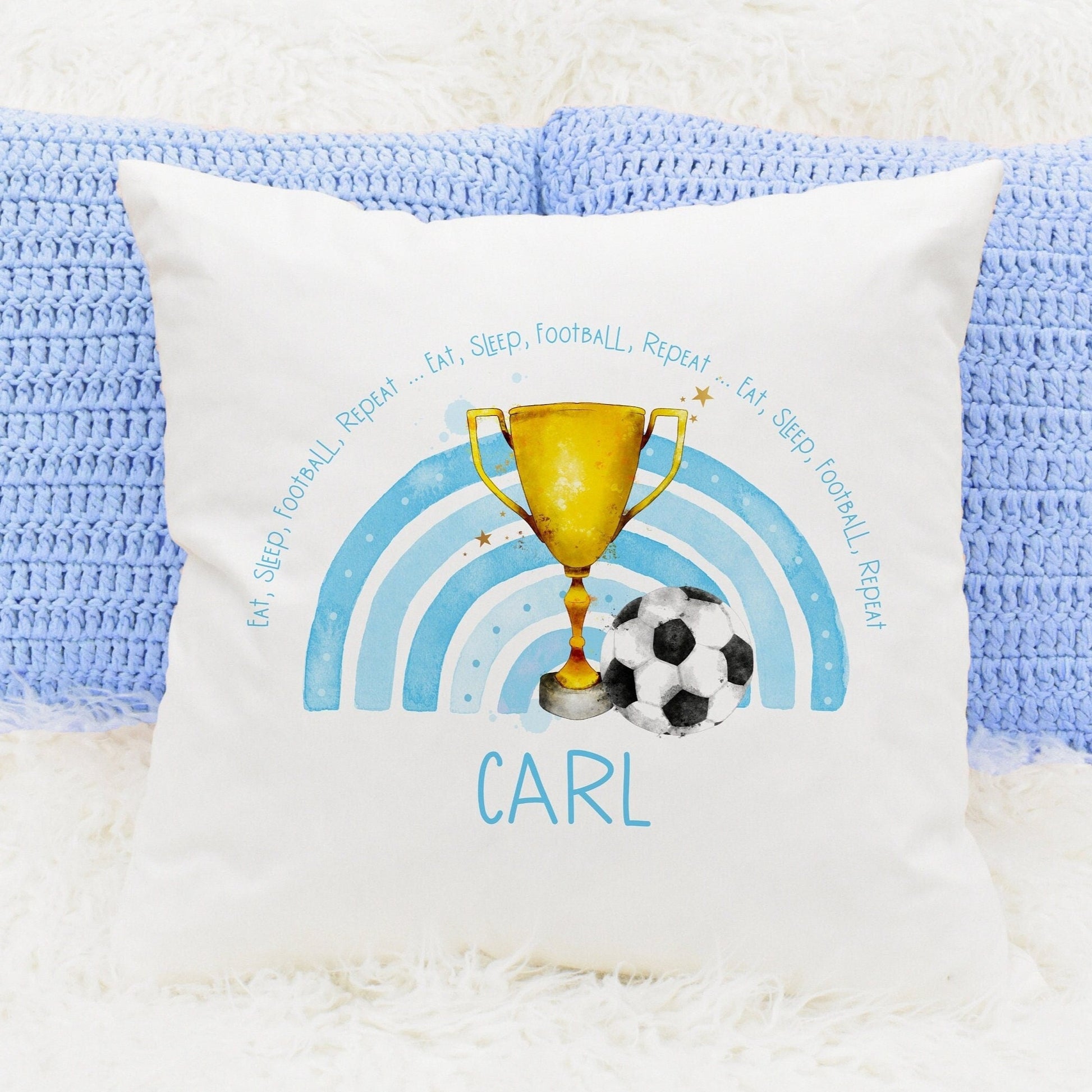 Square cushion featuring a blue rainbow, a trophy and a football. The text reads 'eat, sleep, football, repeat...' Can be personalised