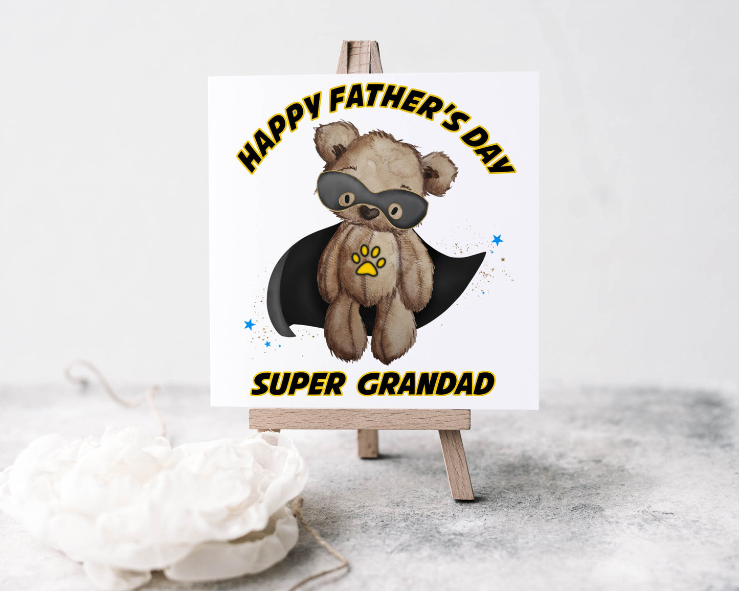 Square greeting card featuring a teddy bear wearing a black cape and a black eye mask design. The text reads 'Happy Father's Day Super Grandad'