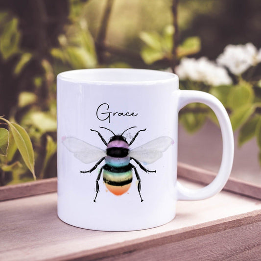 Ceramic mug with the design of a rainbow coloured bumble bee and can be personalised